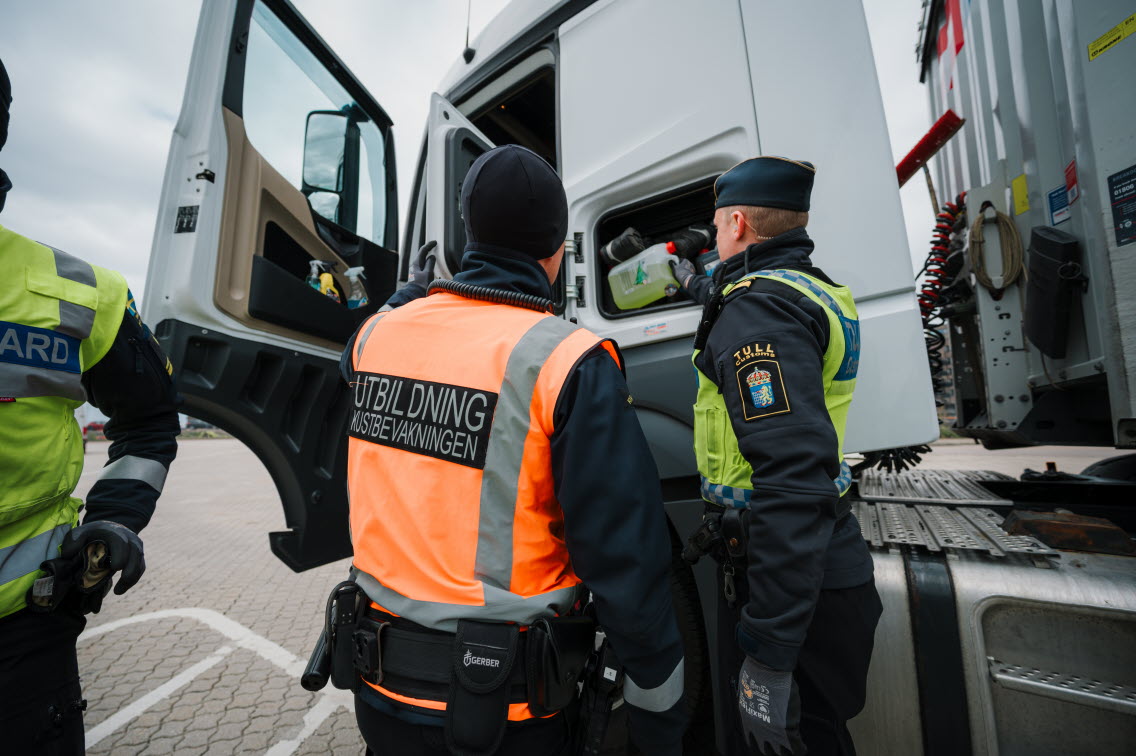 Kustbevakningsaspirant kontrollerar ett litet utrymme på utsidan av en lastbilshytt tillsammans med en tulltjänsteman.